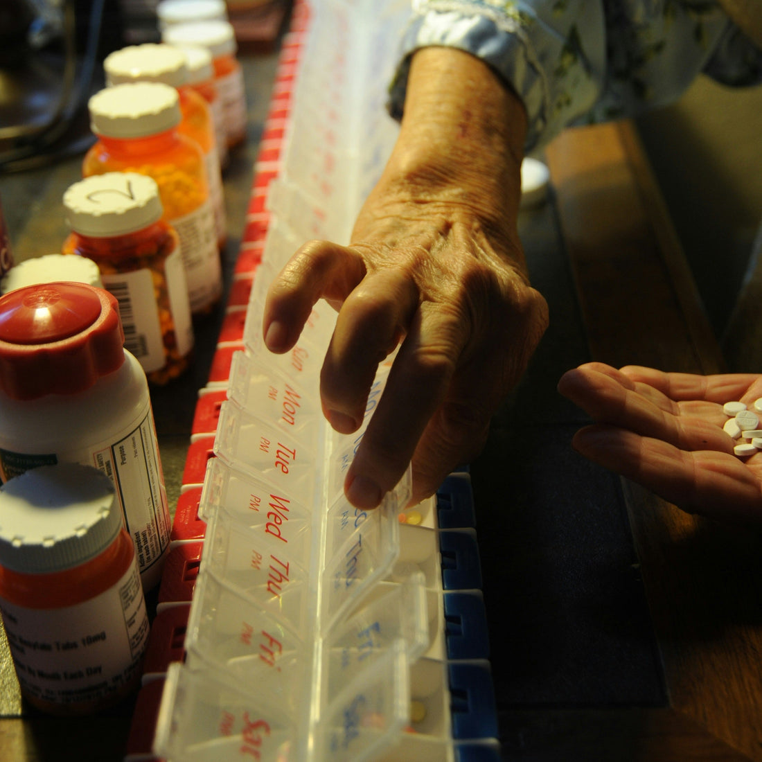 Senior woman organizing daily medications into a weekly pill organizer on a kitchen counter
