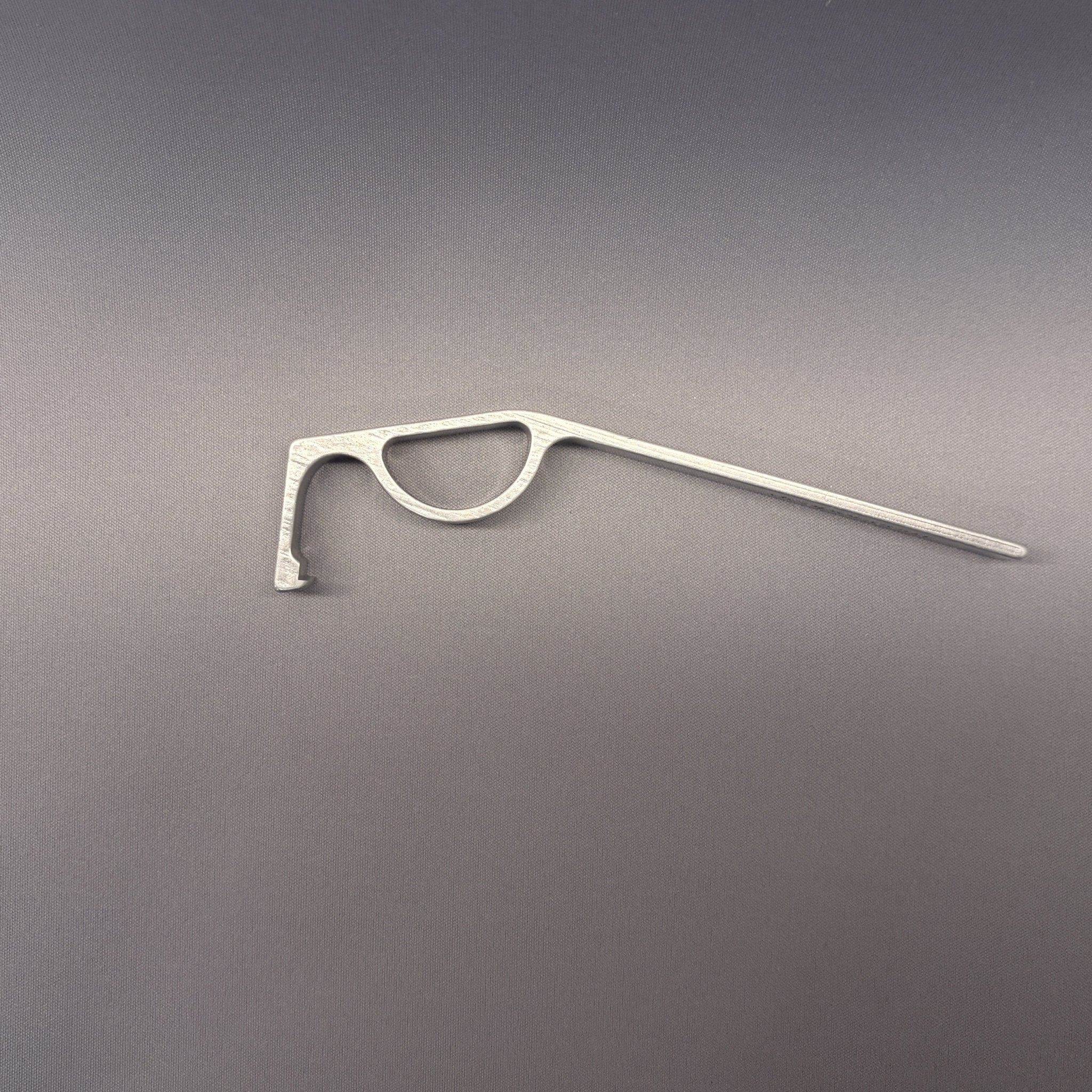 DCAPer childproof cap opener tool — brushed aluminum lever design, flat lay